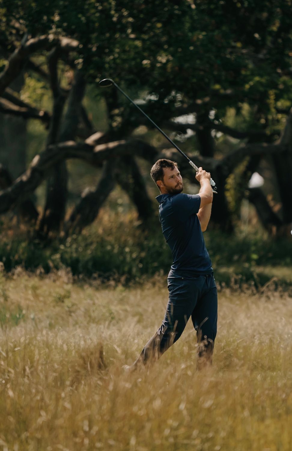Zander following through on a tee shot, tall grass in the foreground